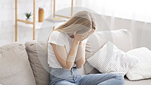 Desperate young woman crying on couch at home