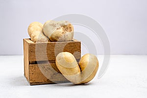 Despicable potatoes of different shapes in a wooden box on a gray background, copy space