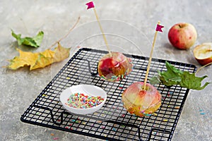 Dessert, caramelized candy apples in transparent caramel, sprinkled with sugar decor, on a black grate on a gray concrete