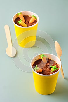 Dessert, carrot cake to go in a yellow paper cup, decorated with cocoa and marzipan carrots on a green plain background. Trendy