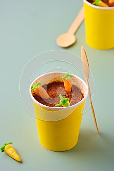 Dessert, carrot cake to go in a yellow paper cup, decorated with cocoa and marzipan carrots on a green plain background. Trendy