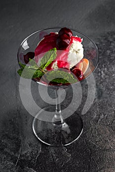 Dessert with Cherry Sauce, biscuits and mint in a martini glass on a grey table and black background. top view