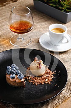 Dessert concept, ice cream and cupcake with berries on a black plate, coffee with brandy on the table