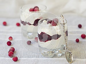 dessert with cranberries and cream in glass on white table, closeup. Healthy food, diet.