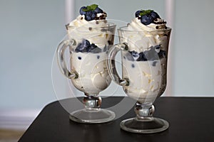 Dessert with cream and blueberries. Decorated with mint. In glass goblets