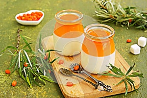 Dessert, creamy panna cotta with sea buckthorn jelly in vintage glass jars on a wooden board or tray on an olive green concrete