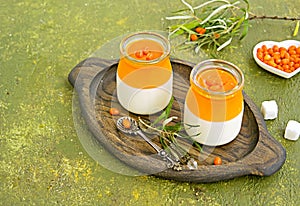 Dessert, creamy panna cotta with sea buckthorn jelly in vintage glass jars on a wooden board or tray on an olive green concrete