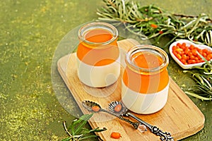 Dessert, creamy panna cotta with sea buckthorn jelly in vintage glass jars on a wooden board or tray on an olive green concrete