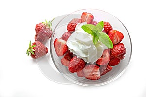 Dessert from fresh strawberries, whipped cream and peppermint garnish in a glass bowl on a white background