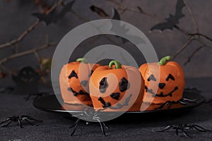 Dessert for Halloween - sweet pumpkin-shaped mousse cakes on dark background with a decor of spiders and bats