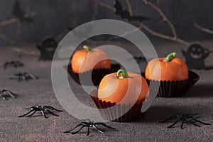 Dessert for Halloween - sweet pumpkin-shaped mousse cakes on a dark background with a decor of spiders and bats