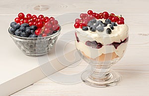 Dessert with mascarpone, cream, and berries in the glass cups on the wooden background.