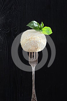 Dessert soft cheese with white sesame on a fork. Photo on a black background. Mint leaves on top. Copy of the space. Vertical