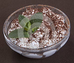 Dessert tiramisu with chocolate and mint leaves in a round glass form.