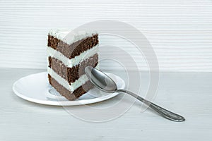 Dessertspoon and a piece of chocolate sponge cake with butter cream are located on the left. White background