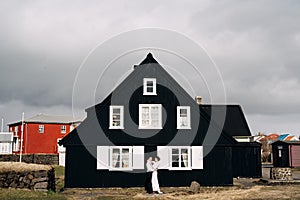 Destination Iceland wedding. Wedding couple near a black wooden house with white windows and shutters. The groom hugs