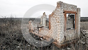 Destroyed and burnt brick structure with a window at the edge of the field