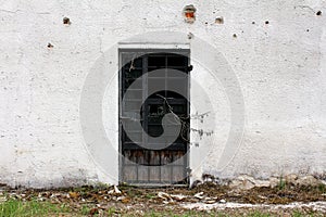 Destroyed cracked closed wooden doors with broken glass on dilapidated old family house white wall surrounded with garbage