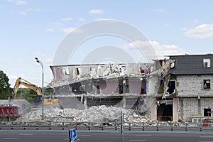 Destroyed house, broken floors, destroyed the walls and roof. Excavator loads construction waste into a red truck. The