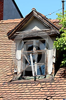 Destroyed old roof window with broken glass and cracked wooden frame mounted on top of abandoned suburban family house