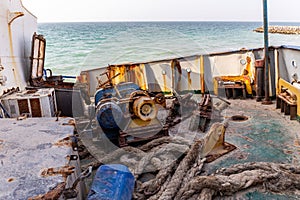 Destroyed and rusty deck of a cargo ship washed ashore, with winch, ropes, machinery and equipment