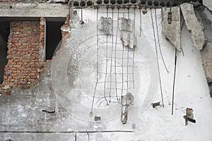 Destroyed white wall with fragments of red brick and concrete stones hanging on the reinforcement. Background