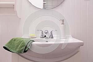 Detail of all white bathroom with sink, porcelain soap dispenser and green bar of soap in dish