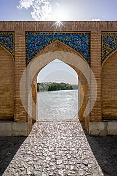 Detail of an arch of a medieval bridge built in islamic, persian style. Sunstar on the top. River view through the arch.