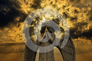 Detail of beautiful bronze statue of an angel with wings against the dark sky with clouds. Beautiful angel with a stormy sky