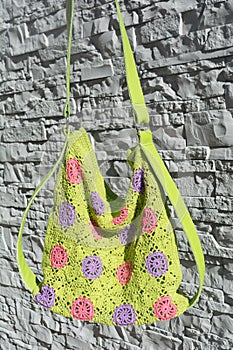 Detail of beautiful colorful crocheted handbag with green handle behind the gray stone wall in the garden in summer