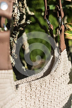Detail of beautiful cream crocheted handbag with brown handle behind the bush in the garden in summer