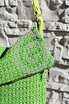 Detail of beautiful green crocheted handbag with green handle behind the gray stone wall in the garden in summer