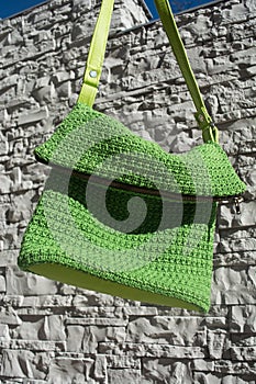 Detail of beautiful green crocheted handbag with green handle behind the gray stone wall in the garden in summer