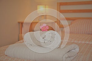 Detail of a bedroom with wooden bed, bedside table, lamp and decorative rolled towels