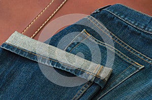 Detail of a blue jeans on brown leather background