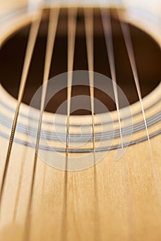 Detail of the body of a light wood guitar, the soundhole and strings