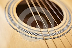 Detail of the body of a light wood guitar, the soundhole and strings
