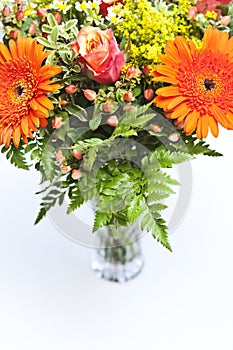 Detail of a bouquet of orange, yellow and red flowers in a vase.