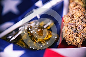 Detail of cannabis CBD oil capsules and bud in front of american