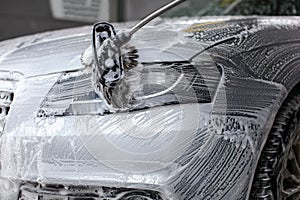 Detail on car front light being washed with soap foam