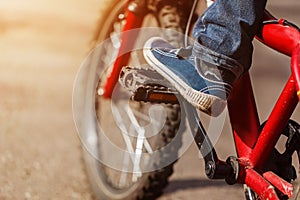 Detail of child cyclist feet riding bike on outdoor in sunny road. Closeup on pedal and foot