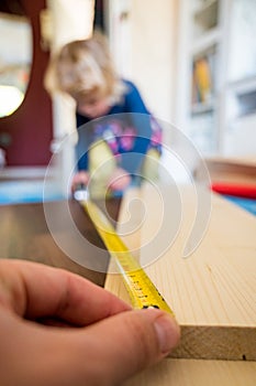 Detail of child helping with measuring wooden plank to make shelves.