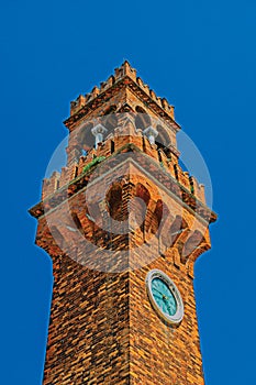 Detail of clock tower made of bricks with sunny blue sky in Murano