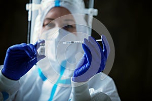 Detail closeup of syringe needle and ampoule , nurse taking injection shot,hands in blue protective gloves holding