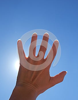 Detail color photography of womans hand catching sun rays and blue sky