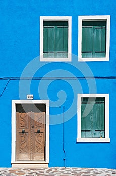 Detail with a colorful house windows and door entrance with blue painted wall and wooden shutters in Burano, Italy