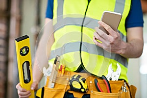 Detail Of Construction Worker On Building Site Wearing Tool Belt Using Mobile Phone