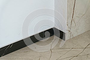 The detail of the corner baseboard on the wall and granite tiles on the floor. A white wall with a copy space, decorated with