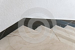 The detail of the corner baseboard on the wall and granite tiles on the floor. A white wall with a copy space, decorated with