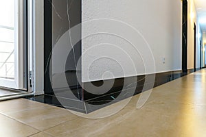 The detail of the corner baseboard on the wall and granite tiles on the floor. A white wall with a copy space, decorated with